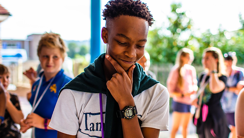 Young person, holding his chin and looking down, while on an Urban Saints Camp this summer