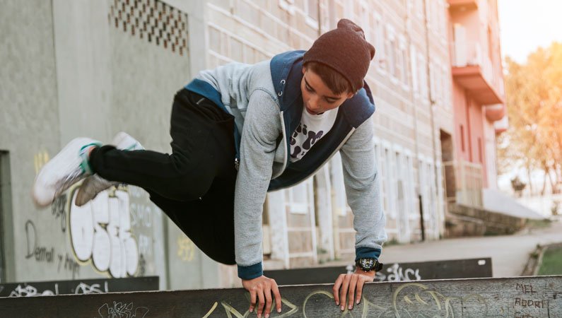 Young person wearing a hoodie and a beanie hat, leaping over a wall - doing some parkour